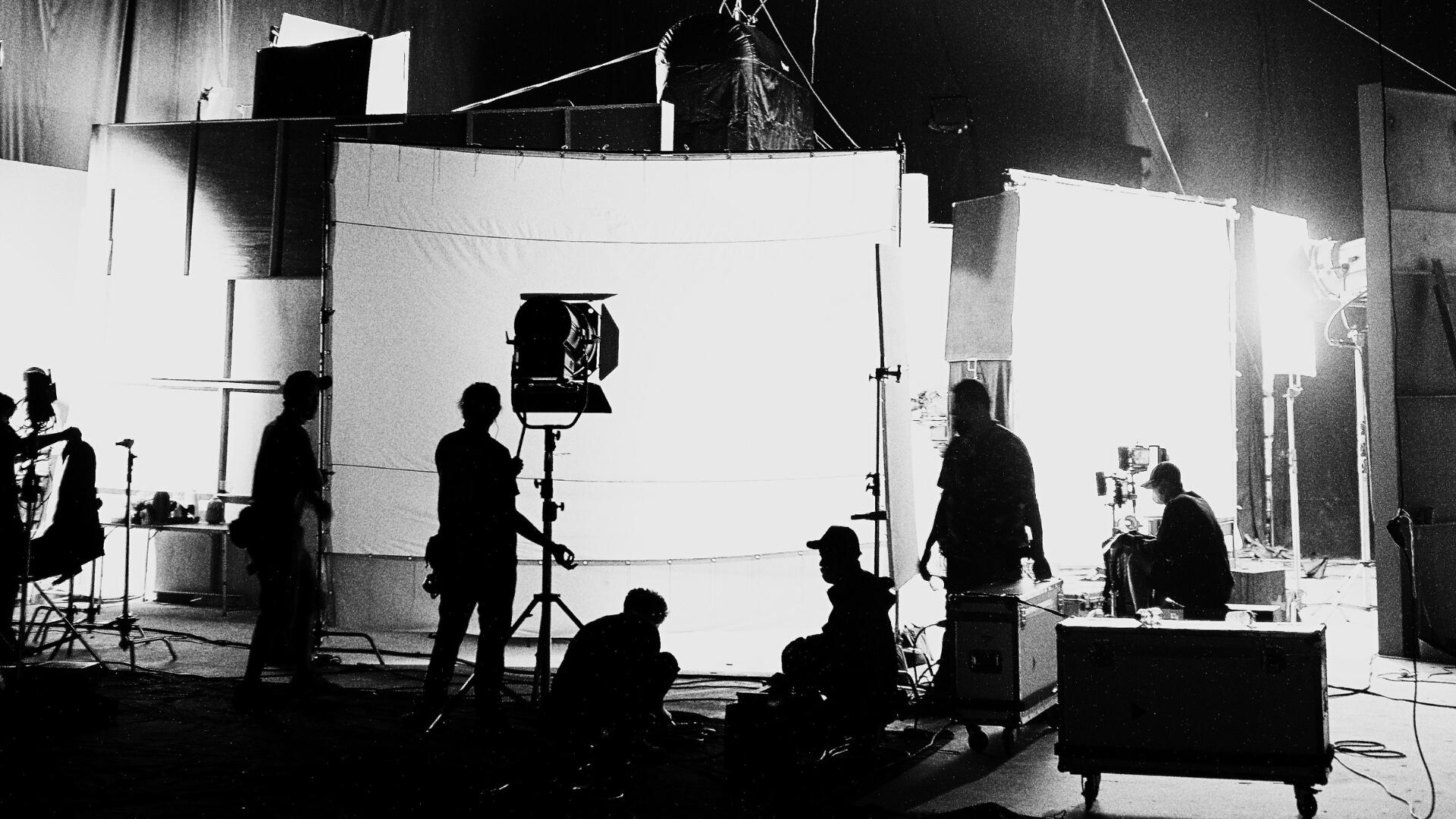 produzione-set-cinematografico Vista ad ampio raggio di un teatrale di posa in bianco e nero con luci di scena e troupe al lavoro
