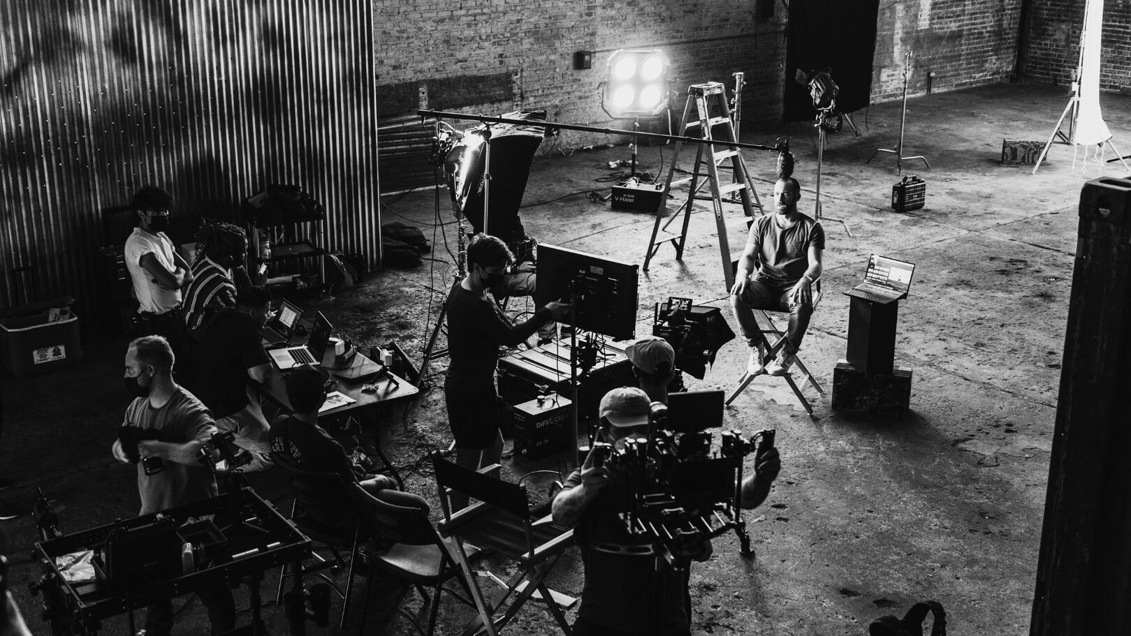 Coordinamento e Logistica di Set — Allestimento e Flussi di Lavoro Vista dall'alto di un set cinematografico in allestimento con luci da studio, sedia da regia, monitor e troupe al lavoro sul campo.